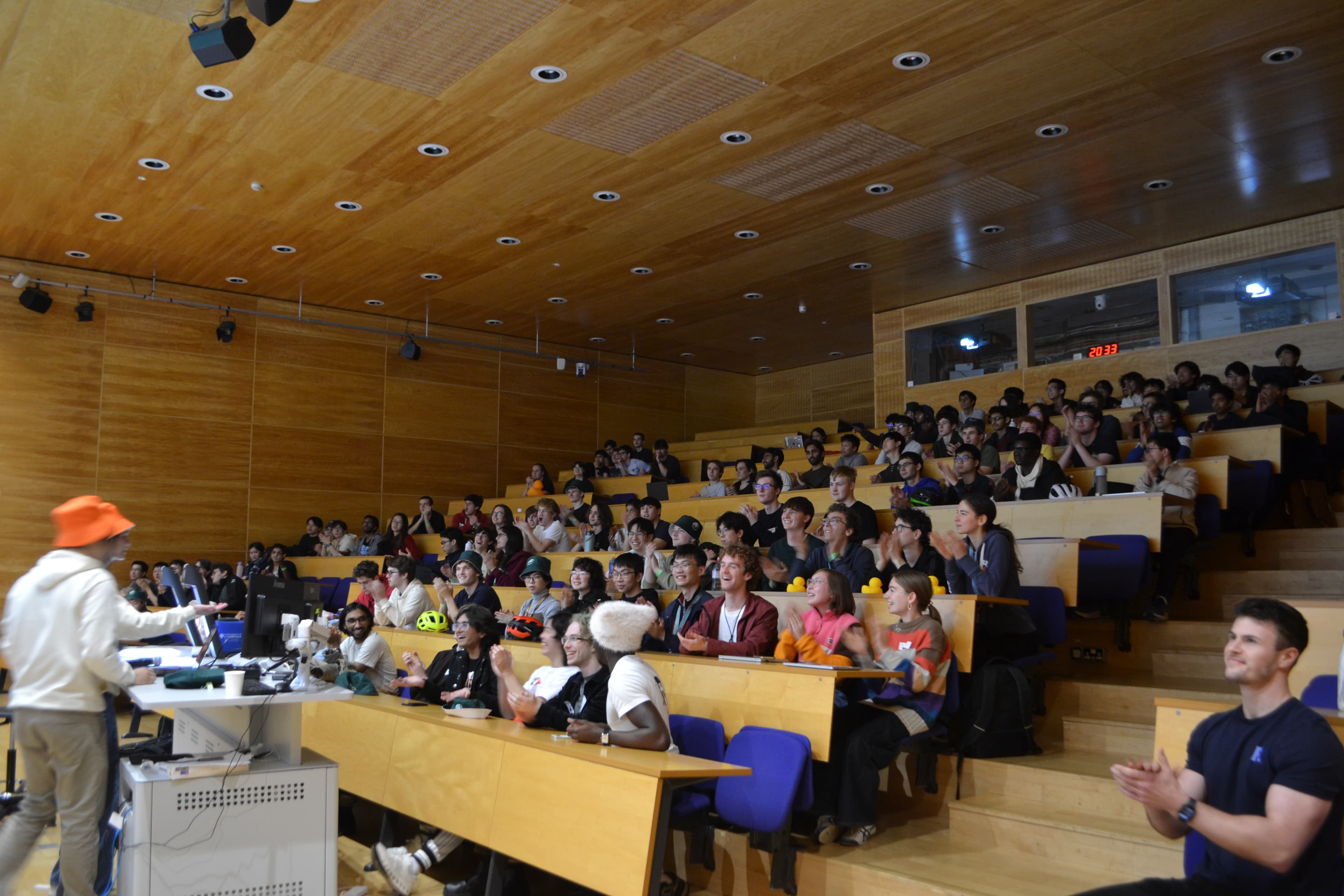 A packed lecture theatre of students laughing and cheering during the CamHack project demos